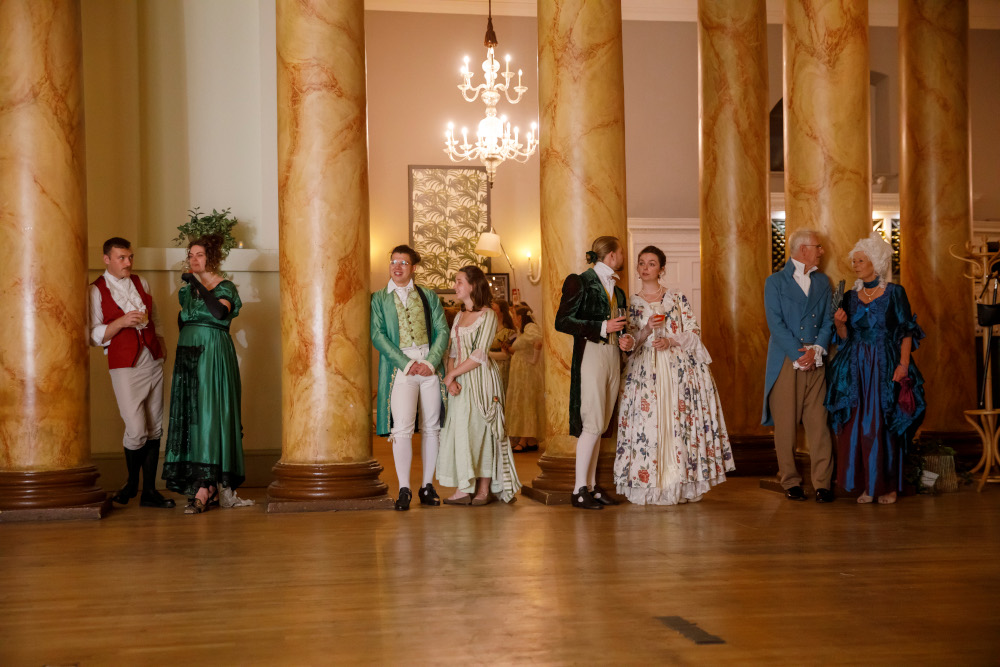 Couples in Georgian costume stand in front of pillars inside York Mansion House