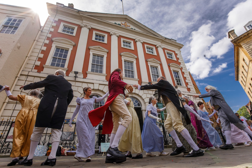 A group of people dancing in Georgian costumes outside York Mansion House